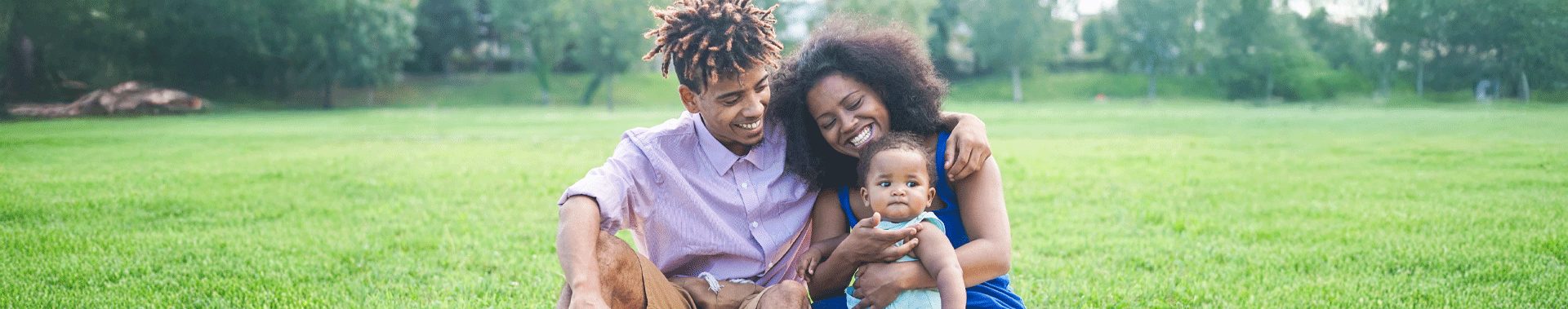 happy african ermian parents with their toddler sitting in a park
